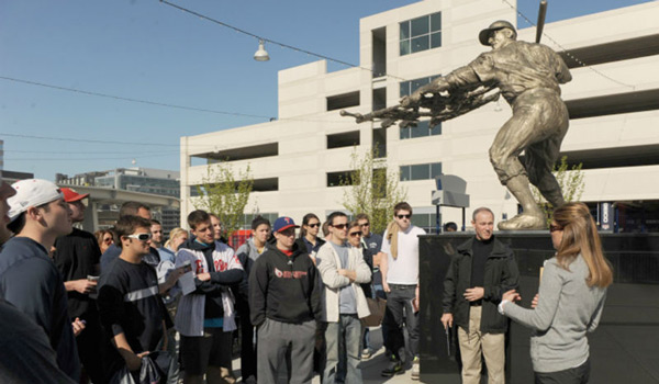 A  class standing next to a baseball statue on a class outing.